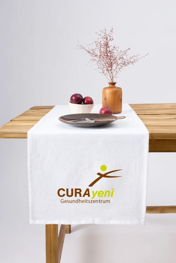 Holztisch mit weißem Tischläufer, Vase mit Zweigen und Teller mit Früchten.